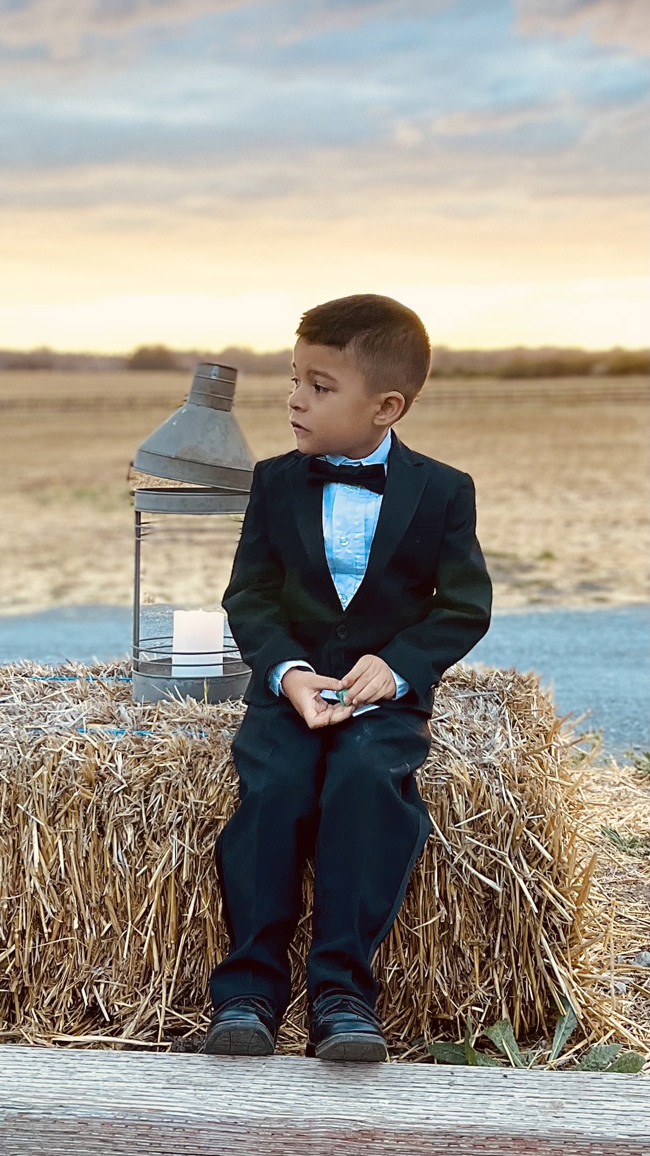 Young boy dressed in a formal tuxedo standing confidently in an open field, adding a touch of elegance to the natural setting.