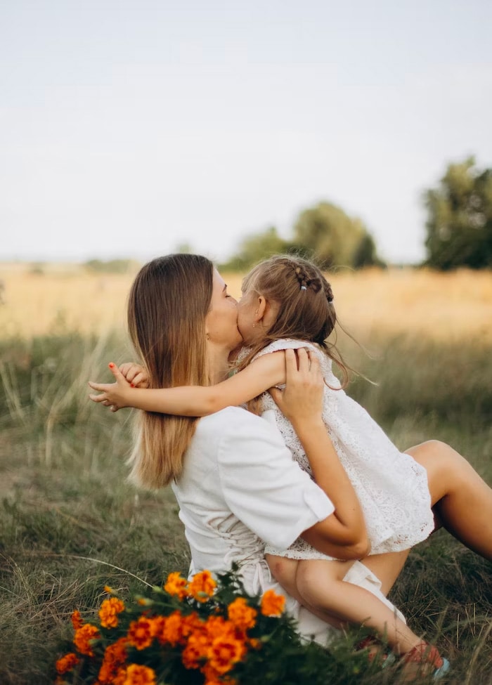 Joyful girl and dedicated nanny embracing and laughing in an open field, capturing a moment of genuine connection and care