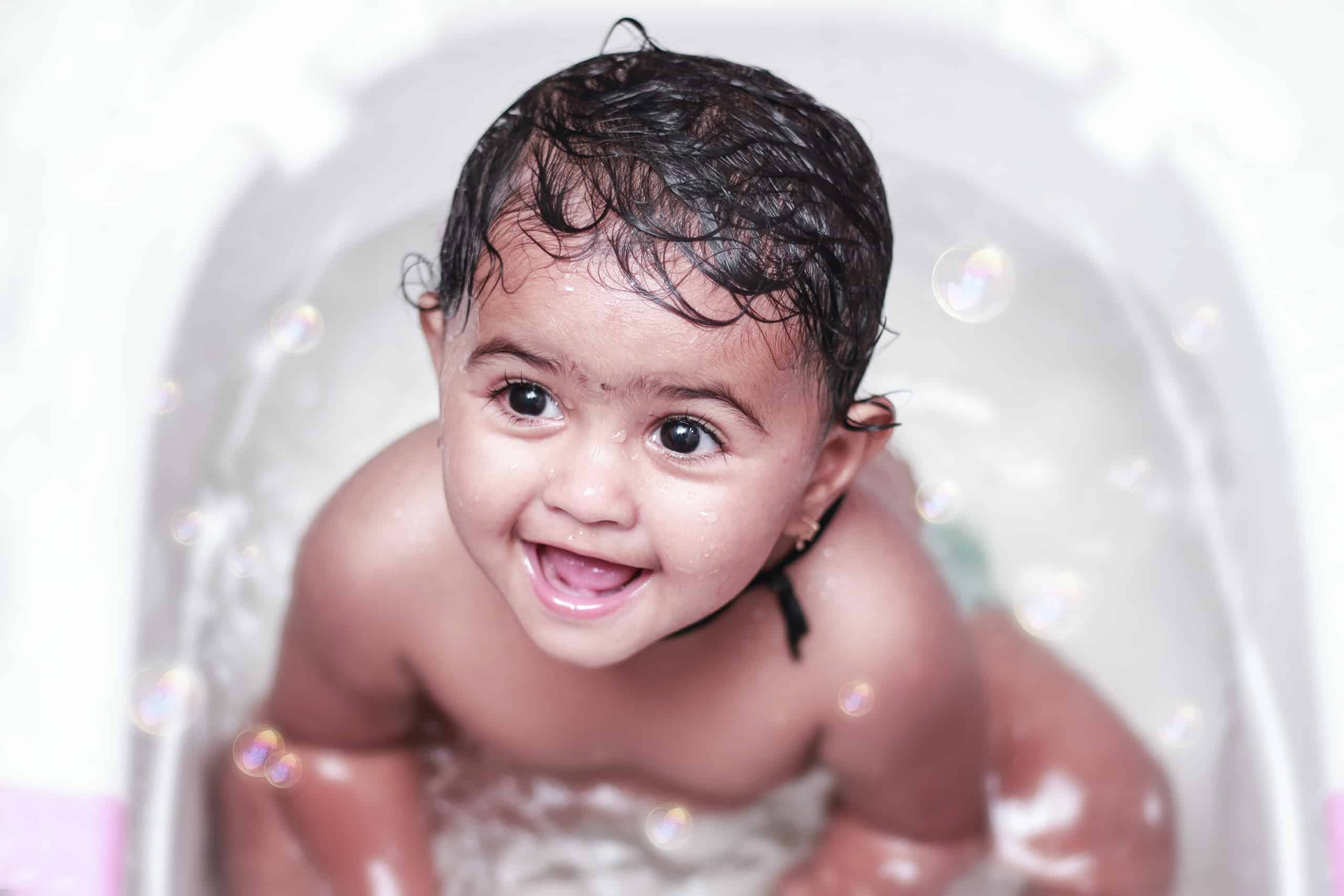 Joyful toddler girl reveling in her bath within a toddler sized tub, beaming with a smile, underscoring Travel'N Tots bath time equipment for comfortable experiences