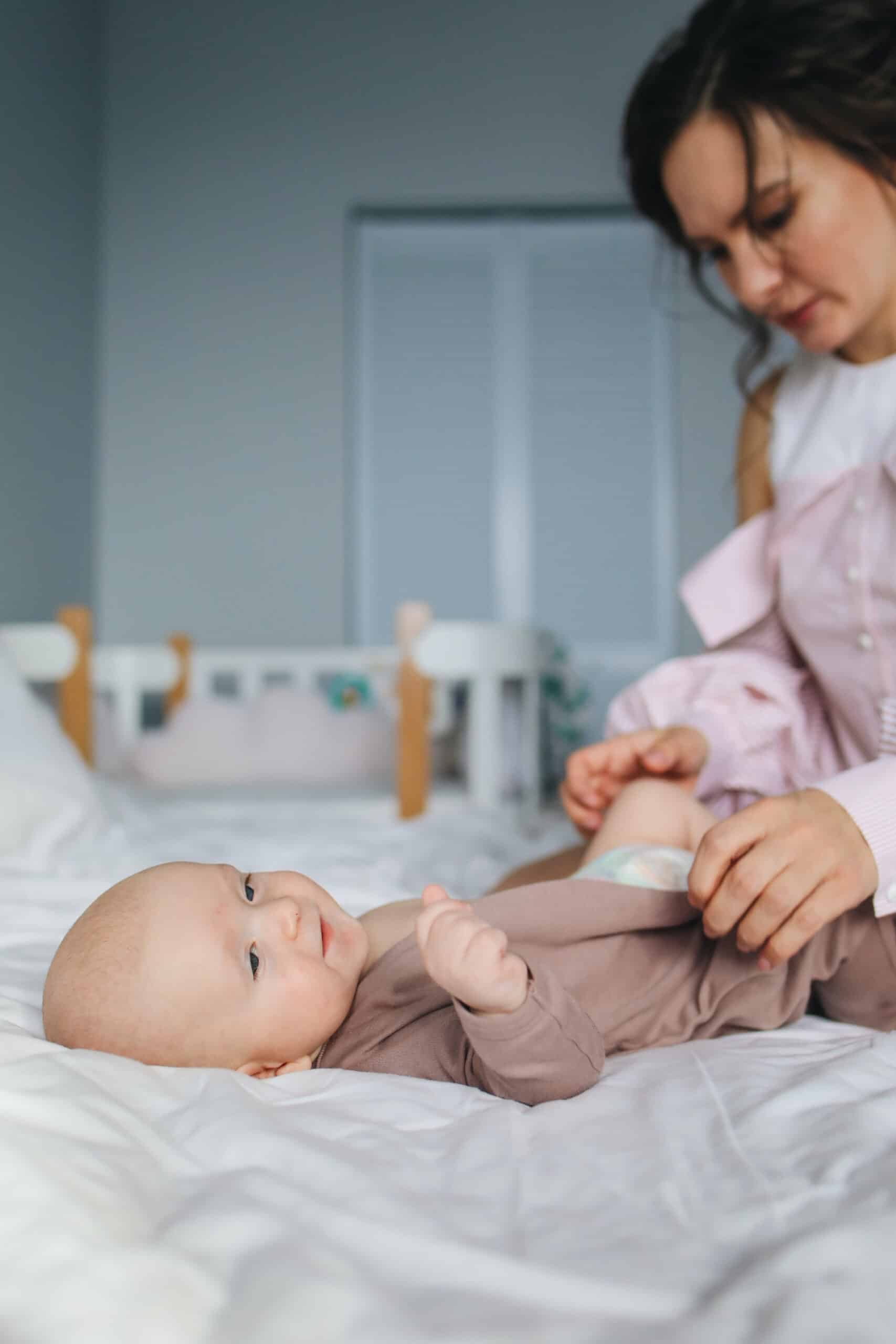 A caring woman gently changing clothes of a content baby lying down, ensuring the infant is comfortable and well-dressed.